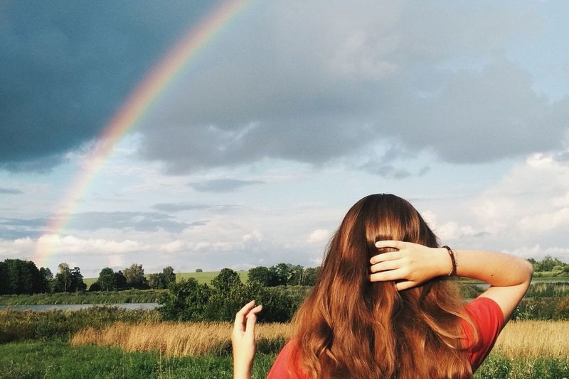 Frau blickt auf den Regenbogen über den Wiesen, während sie ihr Haar/Kopf hält