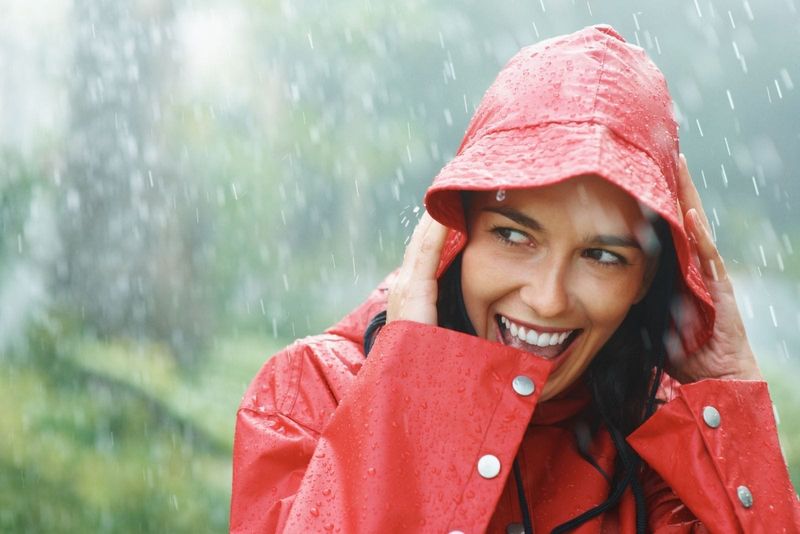 Frau lächelt weiß draußen im Regen und trägt einen Regenmantel