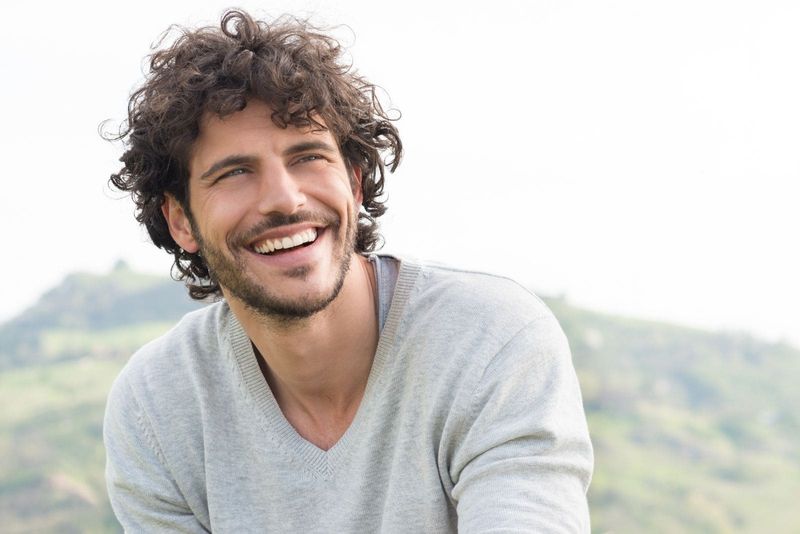 Porträt eines glücklichen Mannes mit lockigem Haar, der draußen sitzt und lächelt