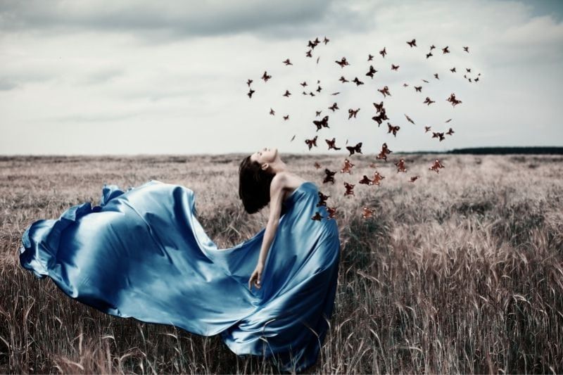 Frau in blauer Satinspitze in der Mitte des Feldes mit fliegenden Schmetterlingen, die eine Herzform bilden