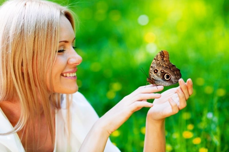 Hübsche blonde Frau, die im Frühlingspark mit dem Schmetterling spielt