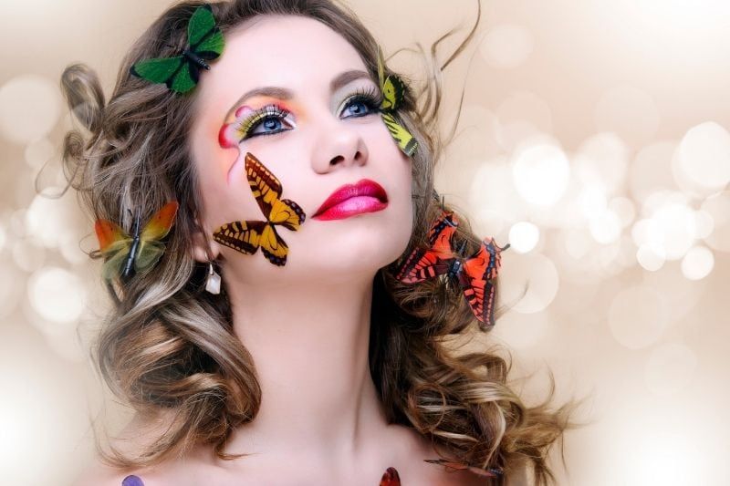 schöne Modefrau mit professionellem Make-up, umgeben von Schmetterlingen in verschiedenen Farben