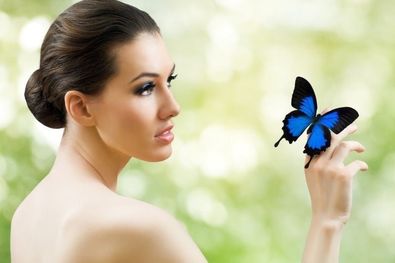 Schöne Schmetterlingsfrau in der Seitenansicht mit einem blauen Schmetterling am Finger