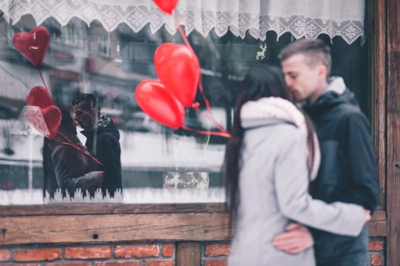 Paar küsst sich mit einem roten Luftballon mit Reflexion auf einem Schaufenster