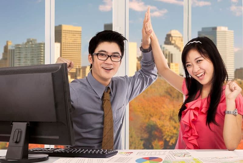 Zwei asiatische Arbeiter feiern, indem sie im Büro in die Hände klatschen