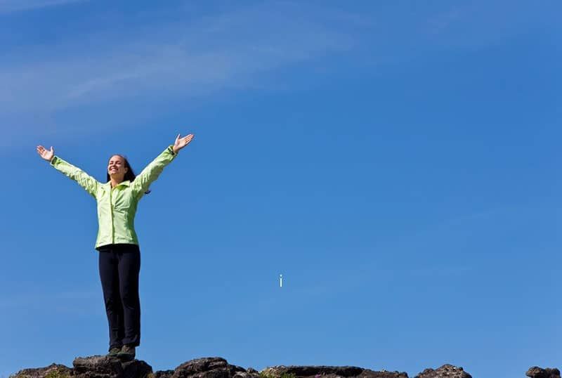 Frau steht mit erhobenen Armen am Horizont und feiert, dass sie den Gipfel des Berges erreicht hat