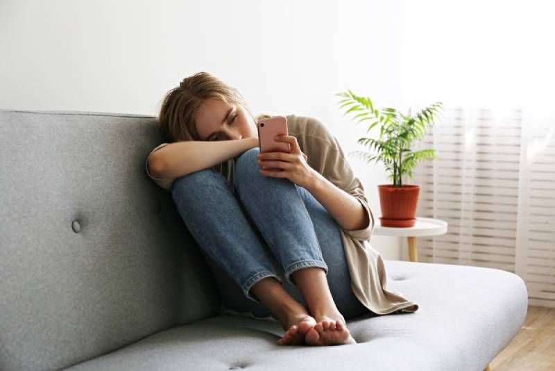 Frau mit depressivem Gesichtsausdruck sitzt und hält ihr Telefon