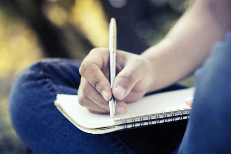 Nahaufnahme eines Mannes, der einen Stift hält und auf ein Notizbuch schreibt