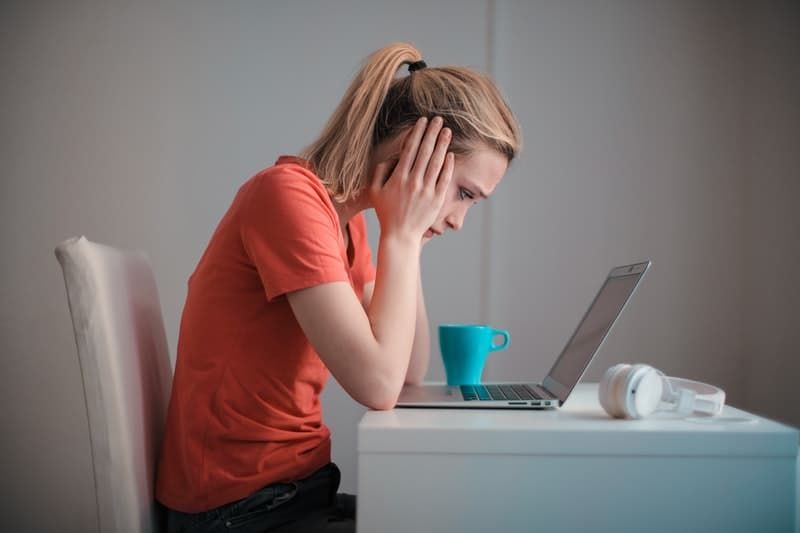 junge Frau mit Blick auf einen Laptop, der tief mit beiden Händen auf ihren Wangen nachdenkt