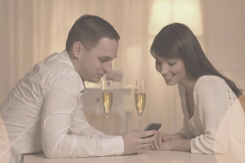 Schönes Paar, das während seiner Wein-Date-Nacht auf das Telefon schaut