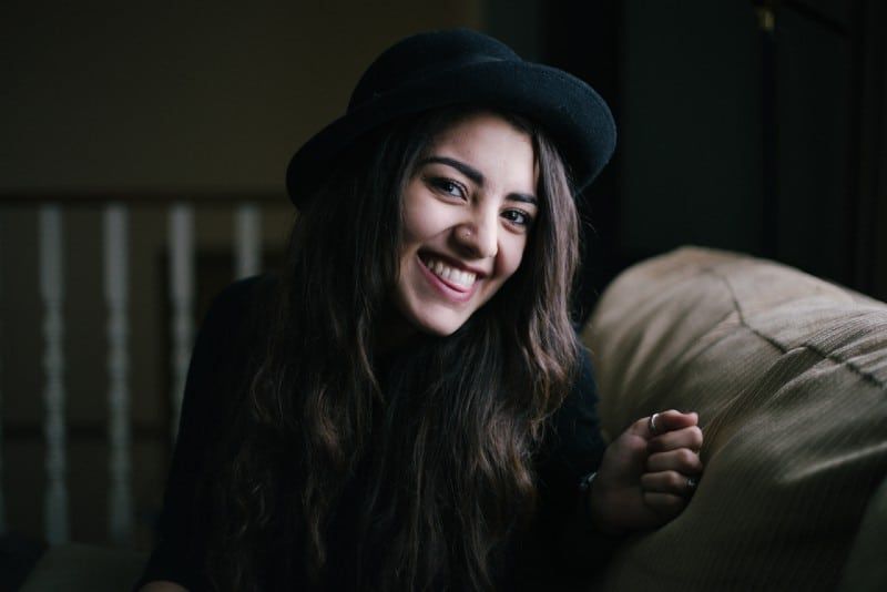 Frau mit schwarzem Hut sitzt auf der Couch und lächelt