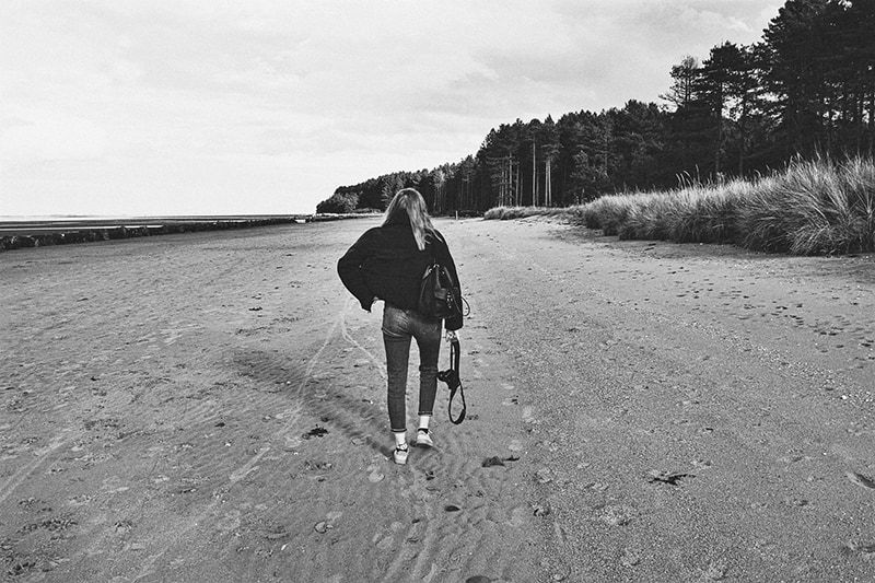 Frau mit Rucksack spaziert am Meeresufer