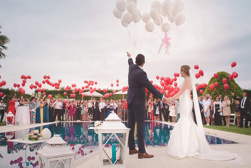 Frischvermählte stehen vor Gästen und halten Luftballons in der Hand