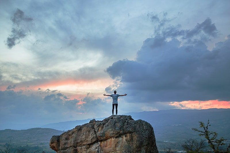 Mann steht während der goldenen Stunde auf dem Gipfel des Felsenberges