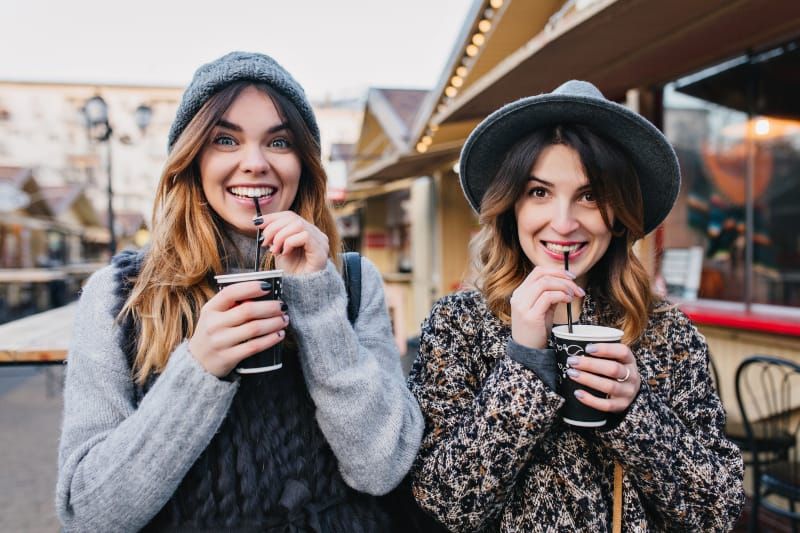 Zwei Freundinnen stehen zueinander und trinken Kaffee aus der Tasse