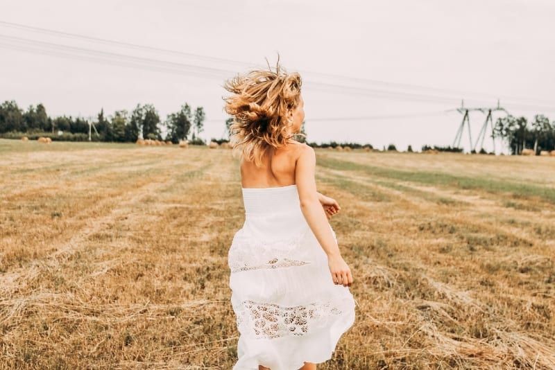 Frau im weißen Kleid läuft auf braunem Feld