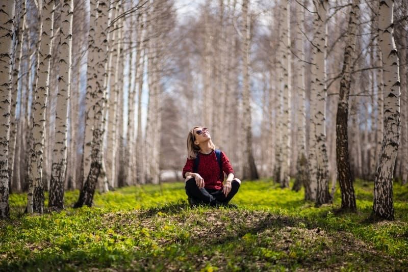 Lächelnde Frau mit Rucksack sitzt zwischen Bäumen