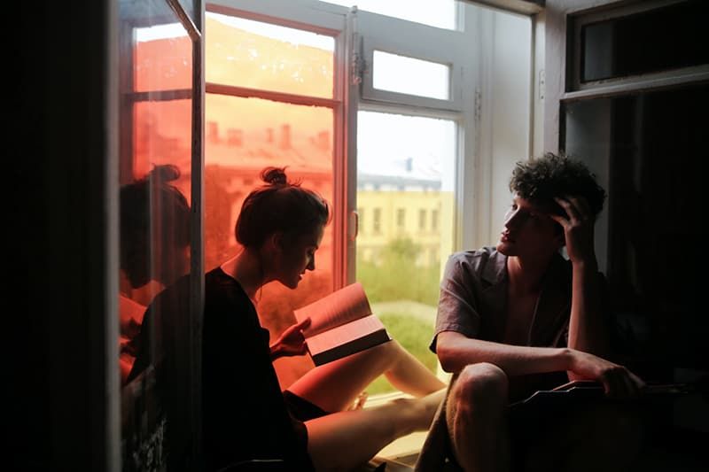 Frau liest ihrem Freund ein Buch vor, während sie auf der Fensterbank sitzt