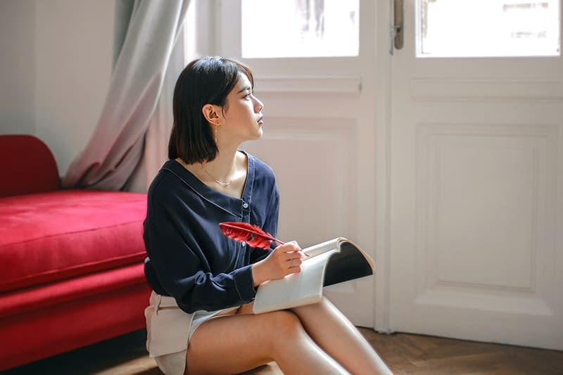 nachdenkliche Frau schreibt in ein Notizbuch, während sie zu Hause auf dem Boden sitzt