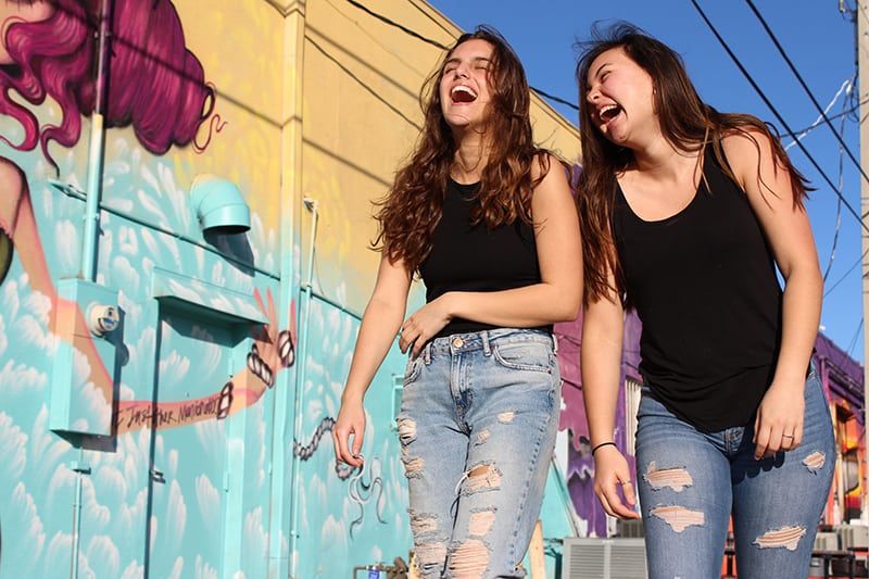 Zwei lachende Frauen gehen an einer Graffitiwand vorbei