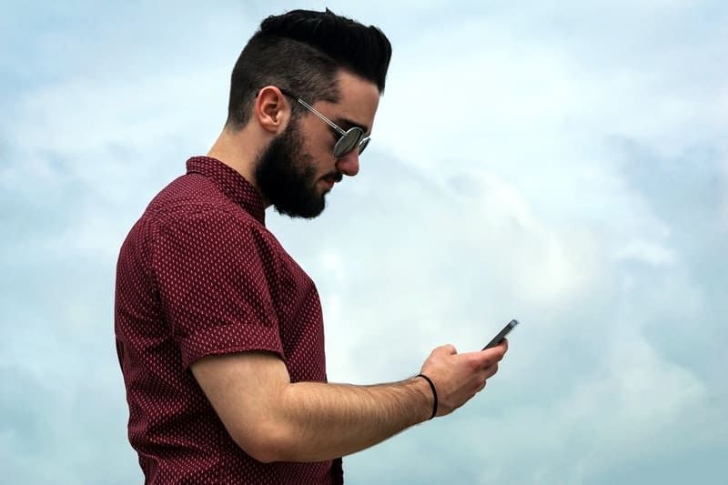 Seitenansicht eines Mannes, der eine Brille trägt und auf sein Telefon schaut