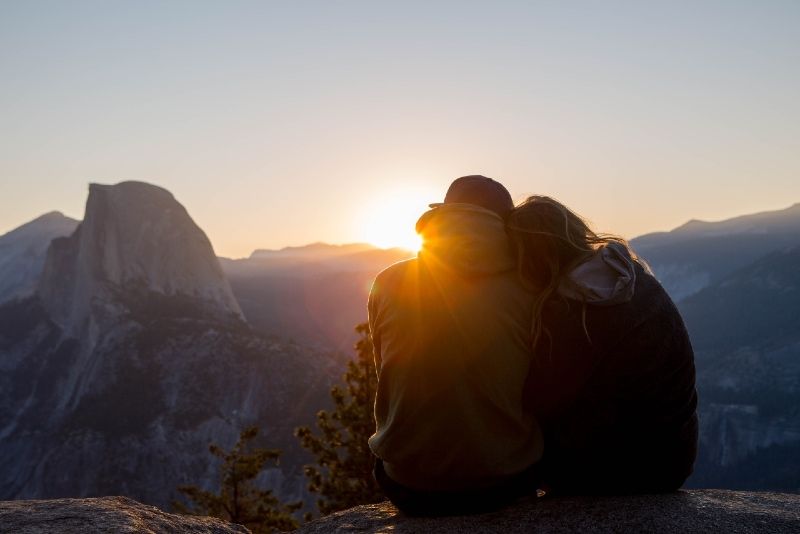 Mann und Frau sitzen bei Sonnenaufgang auf Felsen