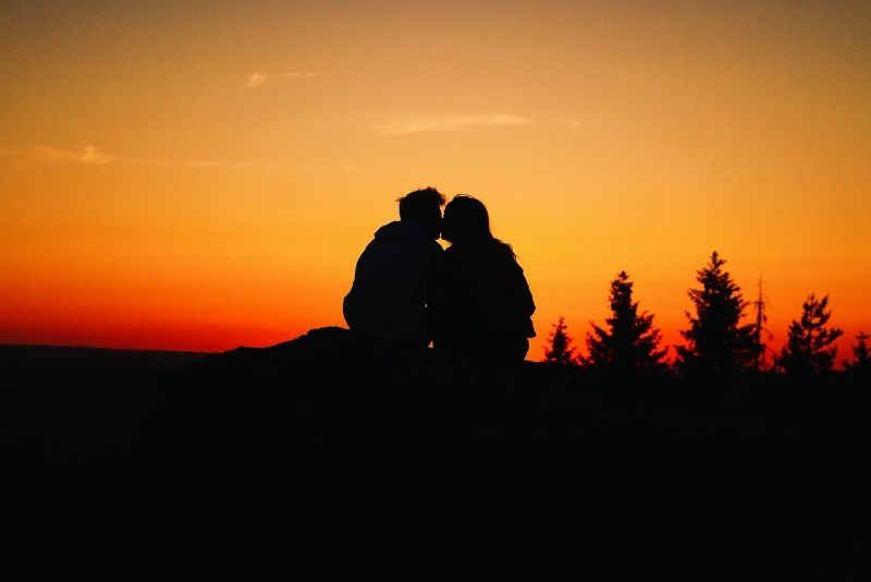 Mann und Frau küssen sich, während sie bei Sonnenuntergang im Freien sitzen