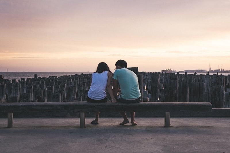 Mann und Frau sitzen auf einer Bank mit Blick auf das Gewässer