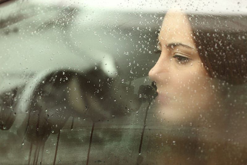 traurige Frau, die durch das regnerische Fenster schaut