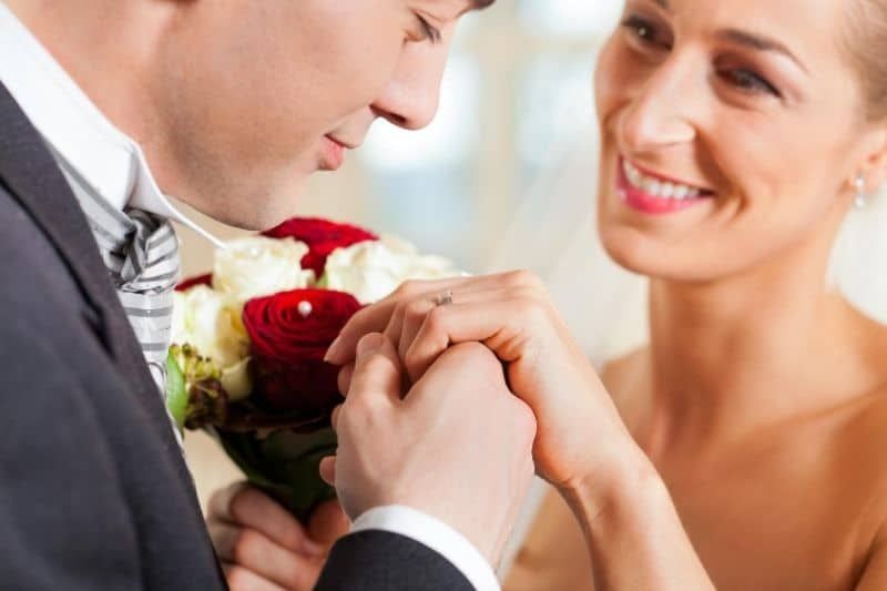 Hochzeitspaar vielversprechender Mann, der die Hand der Frau hält, die einen Blumenstrauß trägt