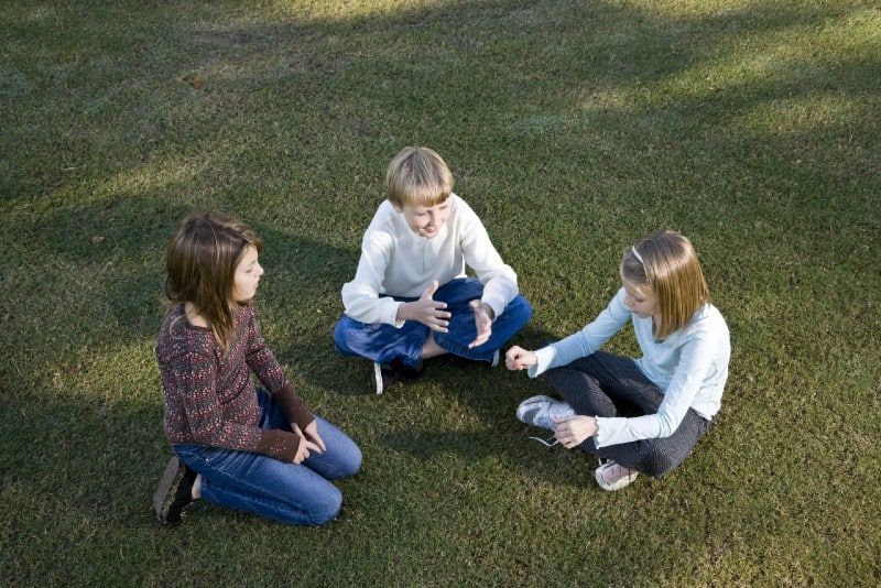 Drei Kinder sitzen im Gras und unterhalten sich