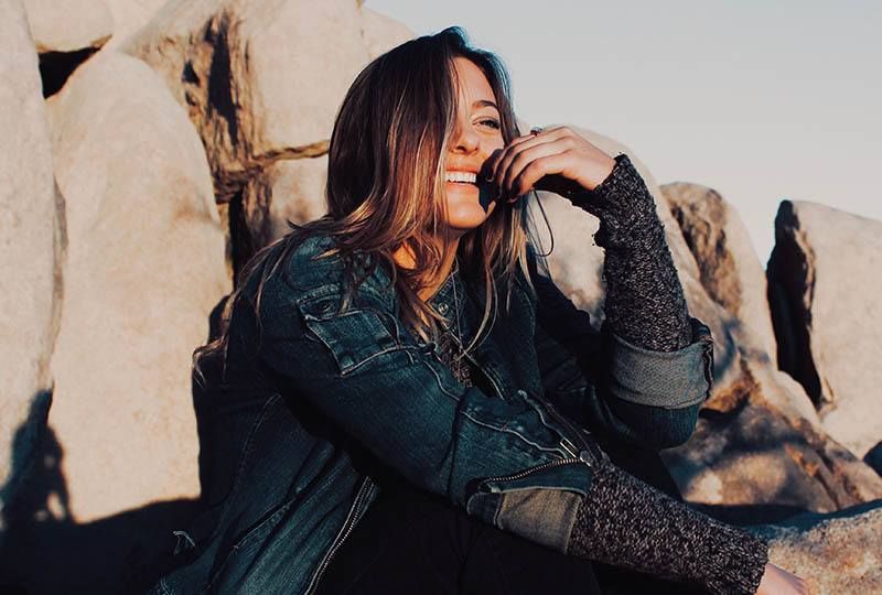 Lächelnde Frau, die draußen auf einem Felsen sitzt