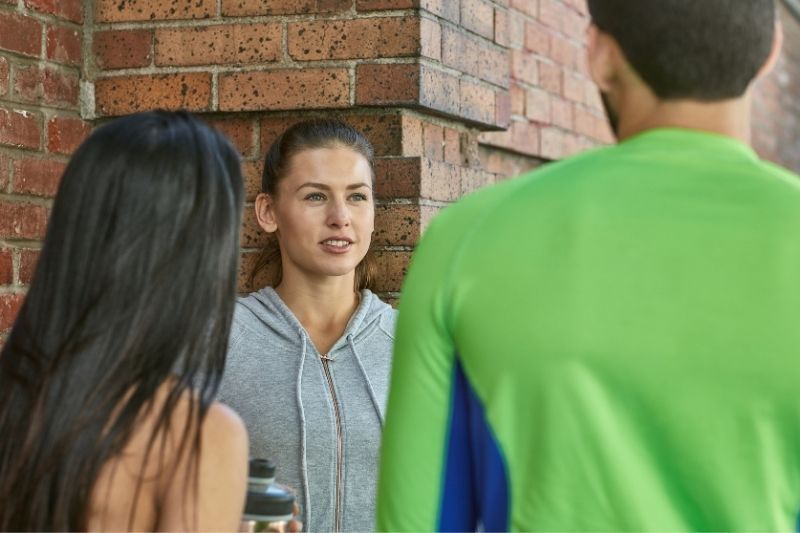Lächelnde Frau, die nach dem Training draußen in der Nähe einer gemauerten Wand mit Freunden spricht