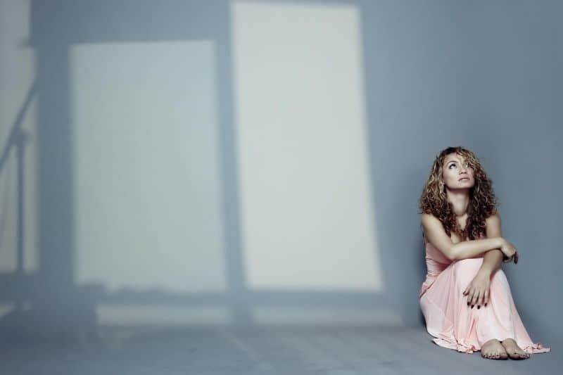 Traurige Frau sitzt drinnen auf dem Boden mit Schatten der Fenster
