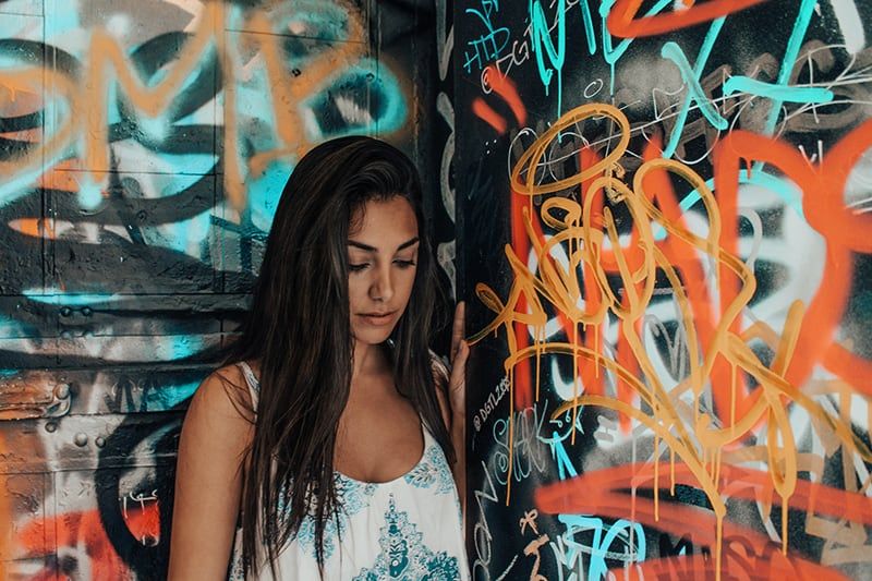 Frau im weißen und blauen Tanktop steht neben Graffitiwand