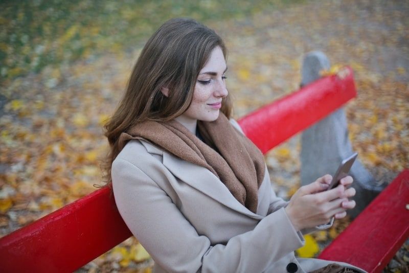 Frau hält Smartphone, während sie auf Bank sitzt