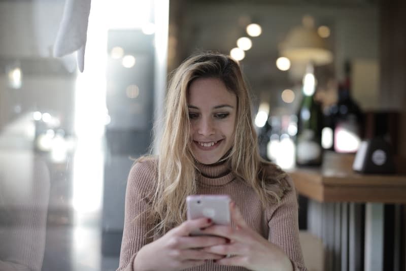 Lächelnde Frau im braunen Strickpullover, die auf das Telefon schaut