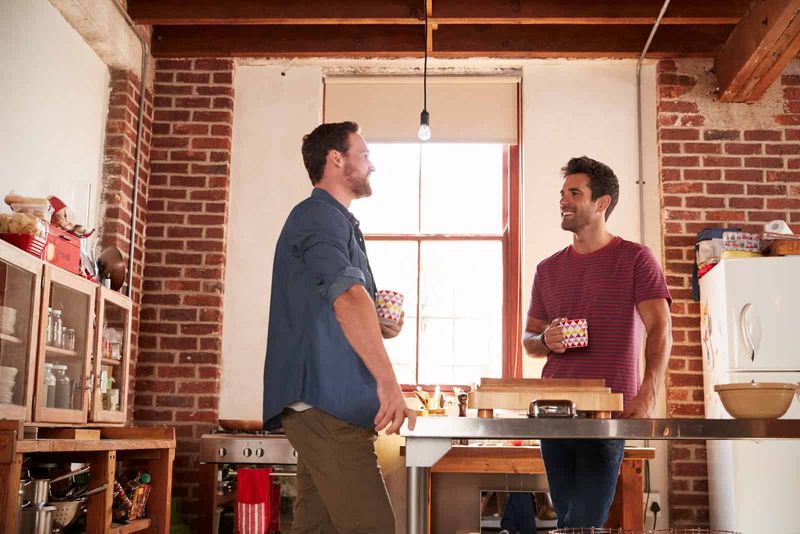 Zwei männliche Freunde stehen in der Küche und trinken Kaffee