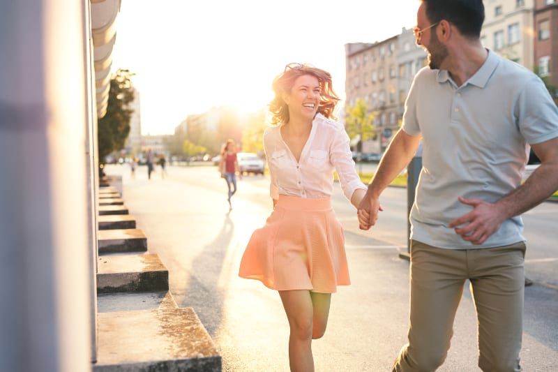 Frau im rosa Rock rennt mit ihrem lächelnden Mann auf der Straße
