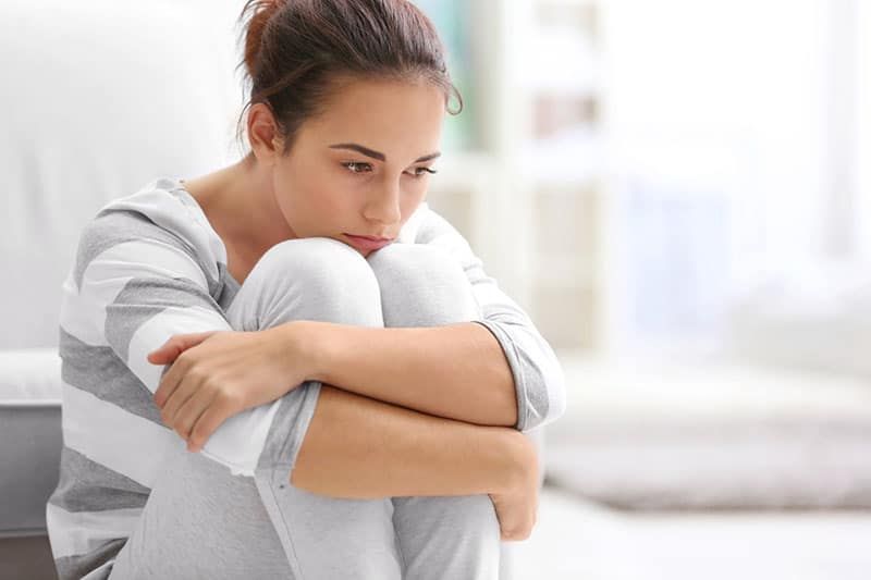 Deprimierte junge Frau sitzt zu Hause auf dem Boden