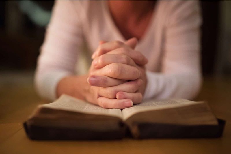 Frau, die mit den Händen auf der Bibel betet