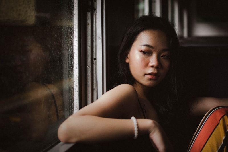 Frau mit weißem Perlenarmband sitzt am Fenster