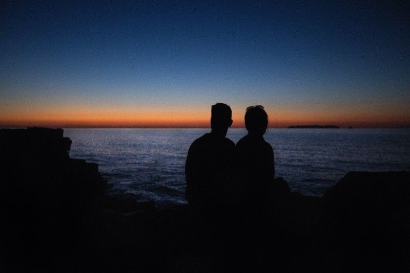 Mann und Frau sitzen auf einem Felsen und schauen aufs Meer
