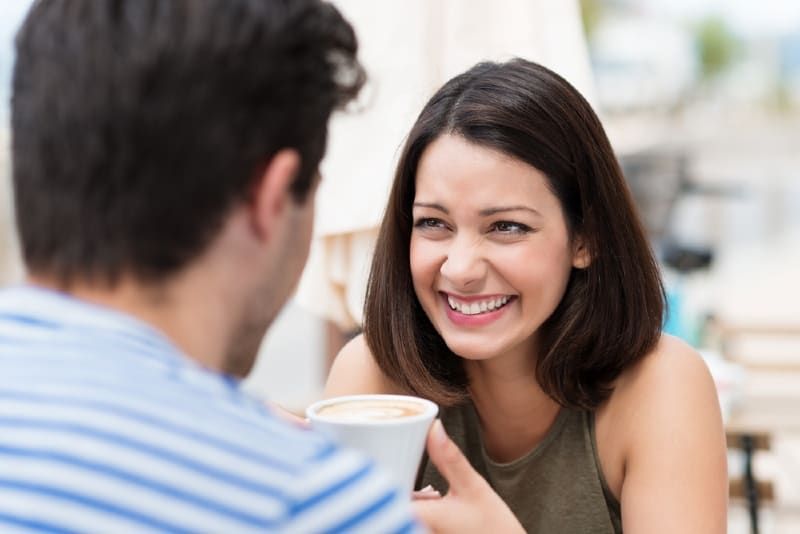 Lächelnde Frau, die den Mann ansieht, während sie eine Tasse Kaffee in der Hand hält