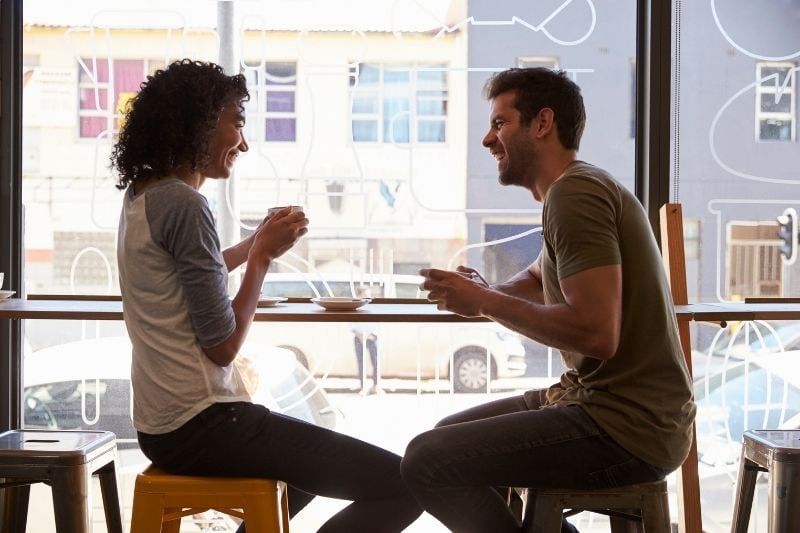 Paar sitzt auf einem Hochstuhl in einem Seitencafé und unterhält sich in der Nähe des Cafés