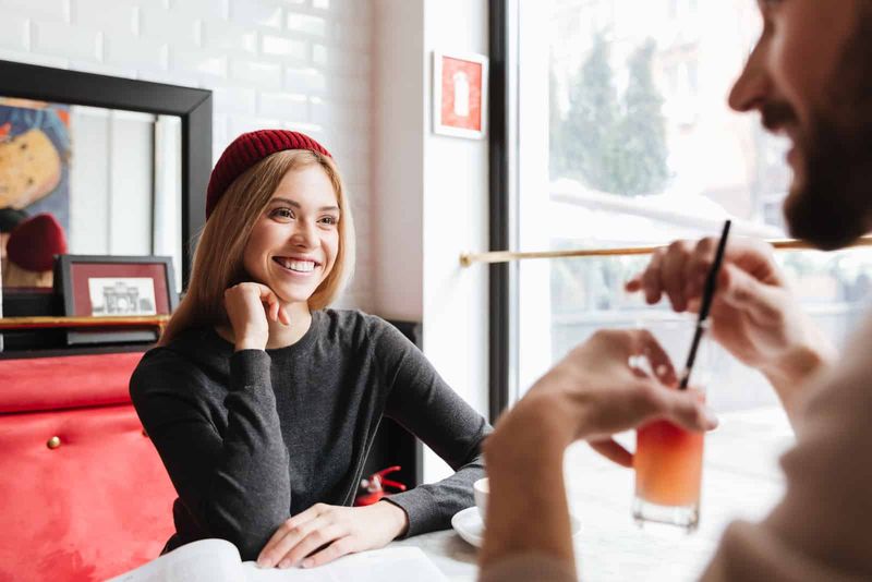 Lächelnde Frau mit rotem Hut, die mit einem Mann am Tisch im Café spricht