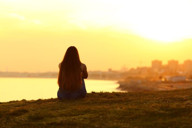 Frau sitzt auf dem Gras und beobachtet den Sonnenuntergang