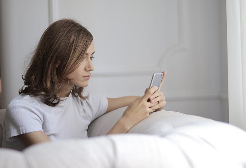 Eine ernsthafte Frau schreibt SMS auf ihrem Smartphone, während sie alleine auf der Couch sitzt