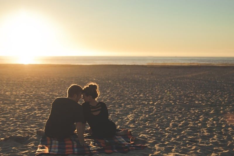 Mann und Frau sitzen bei Sonnenuntergang am Strand