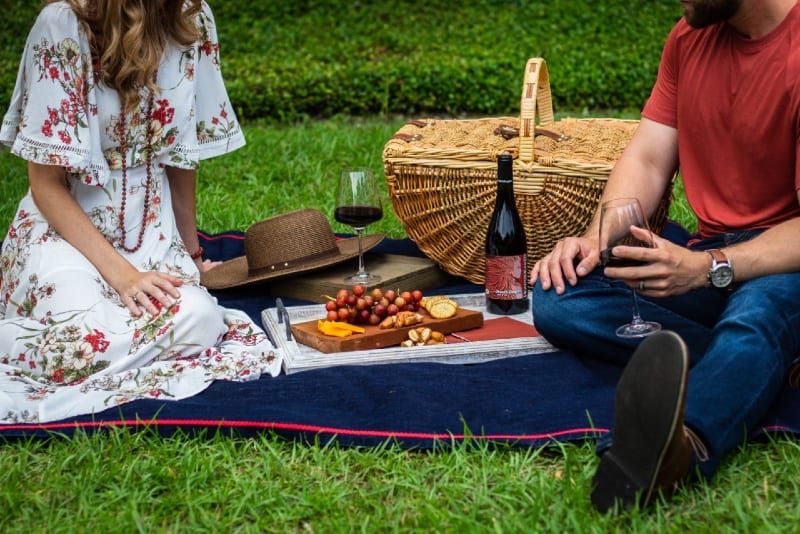 mann und frau sitzen auf textil in der nähe von picknickkorb